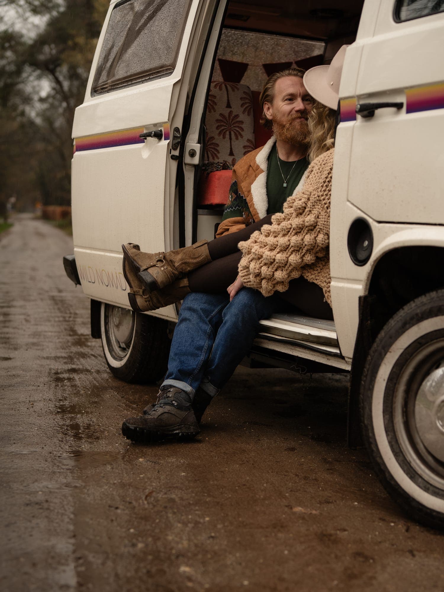 Een stel zit dicht tegen elkaar in de open deur van een oud busje in het bos