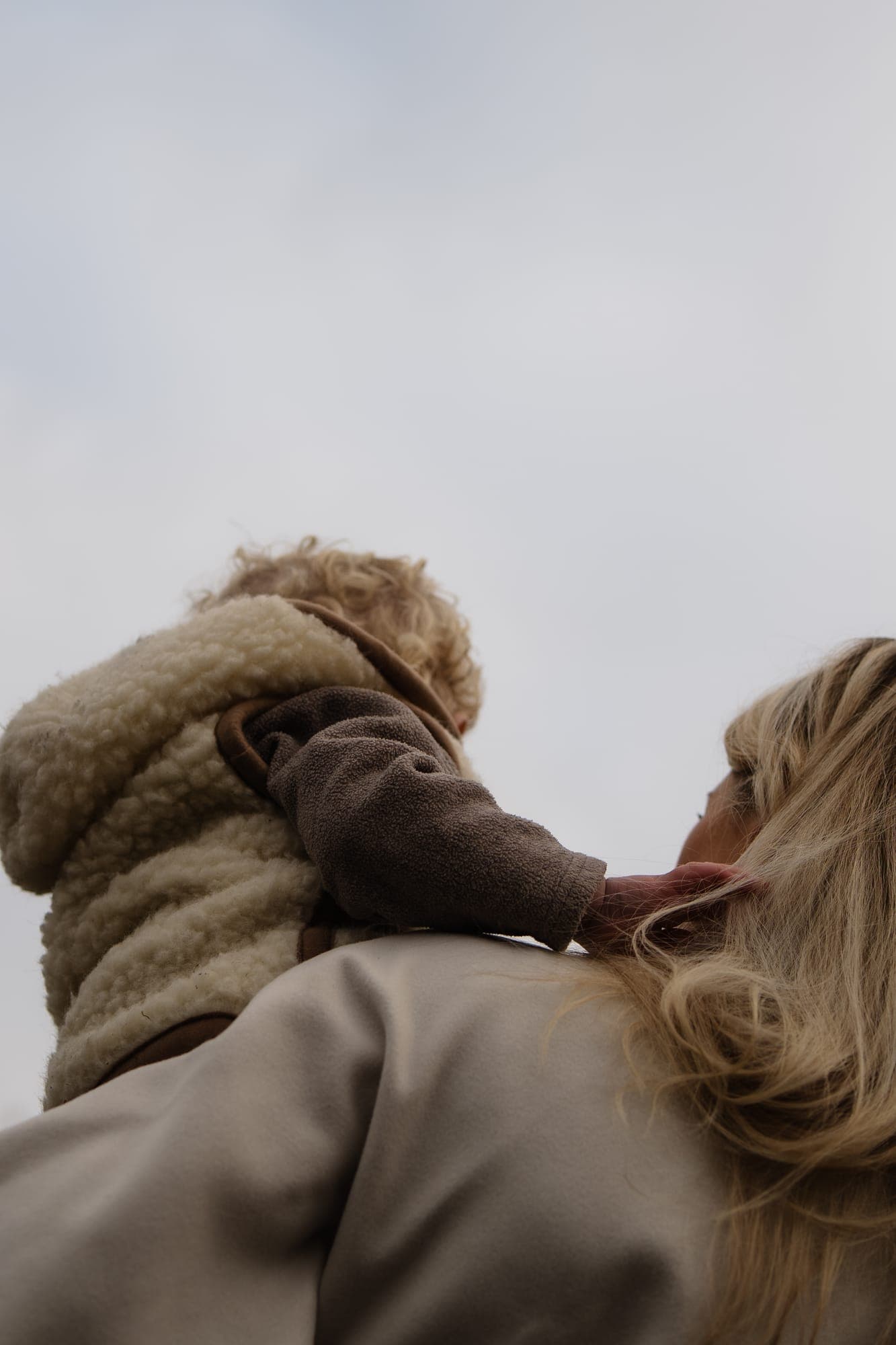 Een kind op de schouders van zijn moeder, van onderen gefotografeerd tegen de lucht