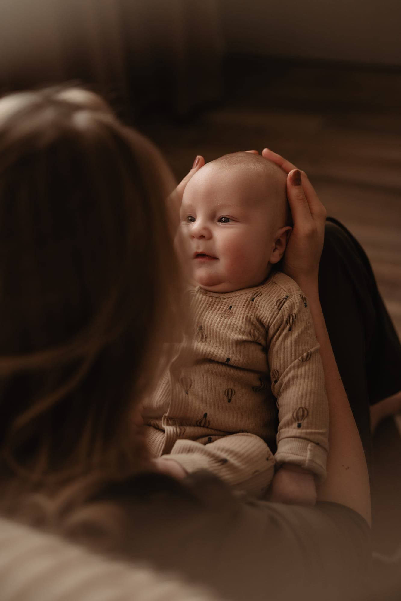 Een newborn kijkt glimlachend naar zijn moeder, die zijn hoofdje vasthoudt