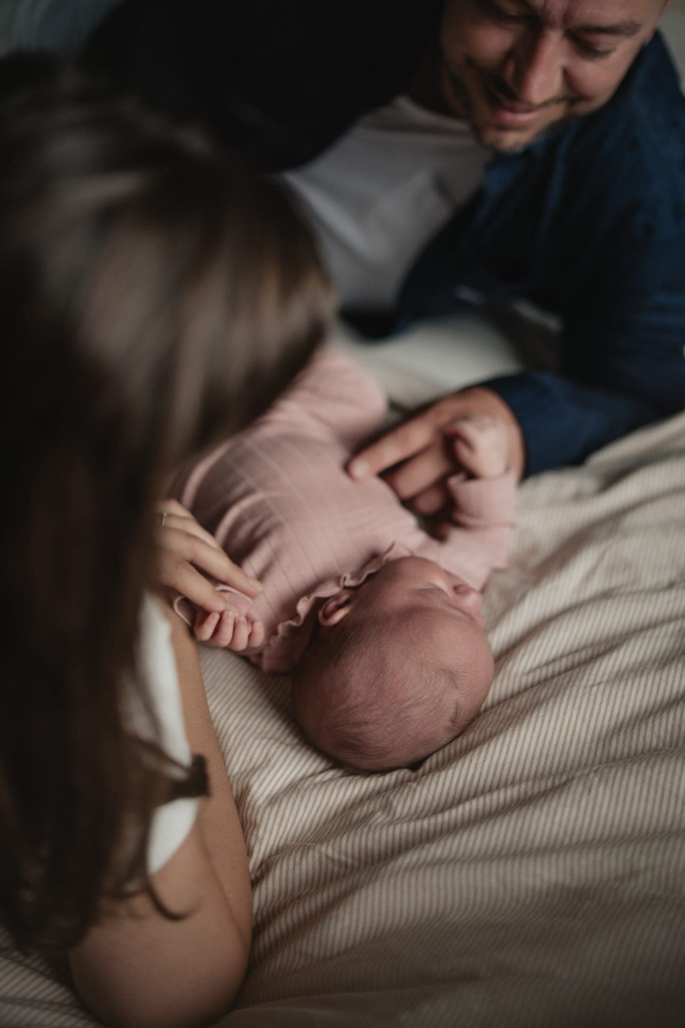 Ouders buigen zich op bed over hun newborn in een roze pakje