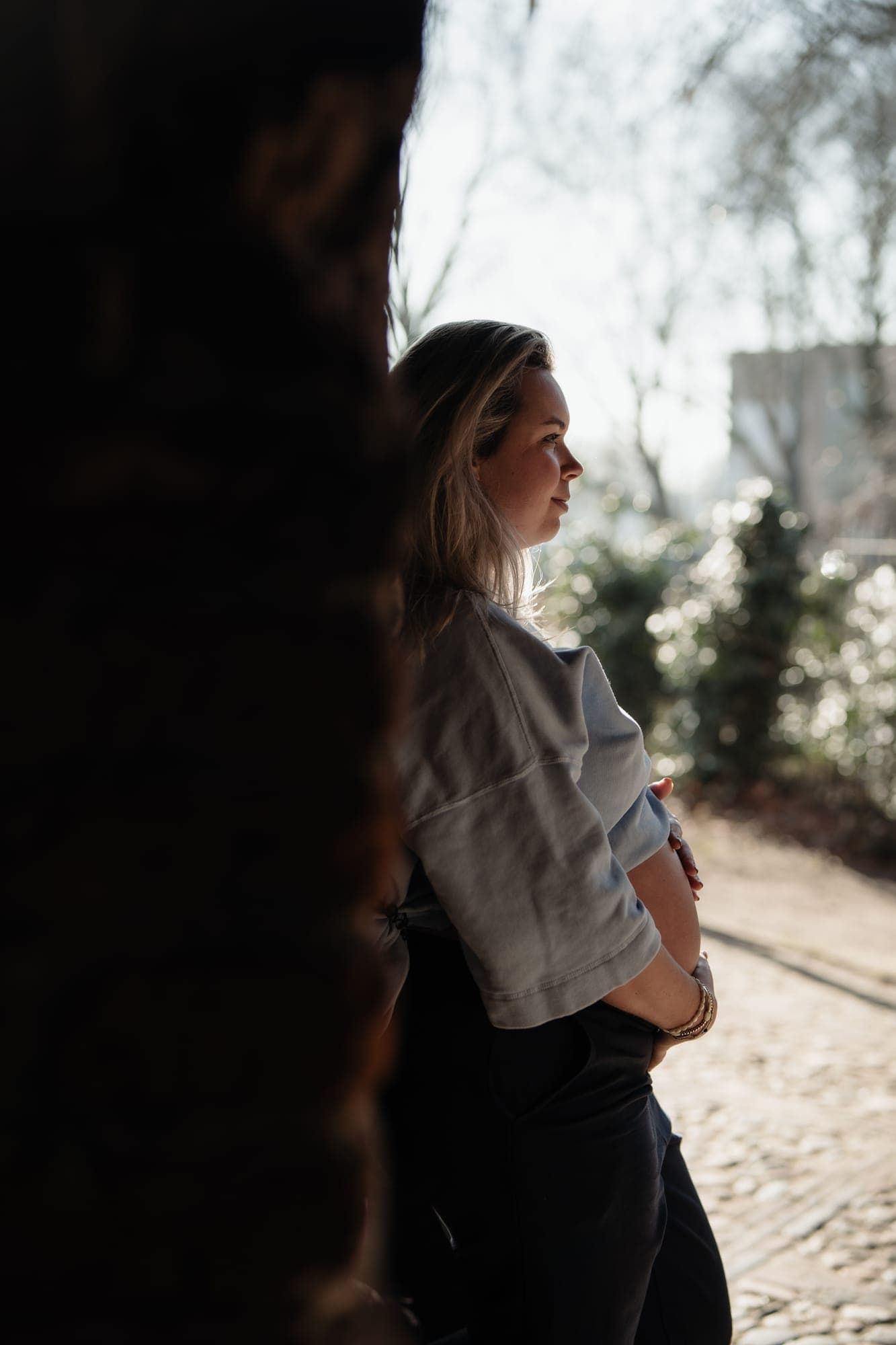 Een zwangere vrouw in profiel in de schaduw van een poort, met licht op haar gezicht